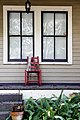 A lonely red chair decorated with Mardi Gras beads sits on a porch.