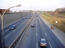 an 8-lane roadway from an overhead bridge with three parallel train tracks on the right