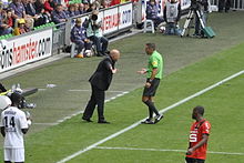 Photographie de deux hommes en discussion sur un terrain en herbe