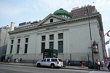 The building's marble facade as seen from across 14th Street. There is a white SUV parked outside the building, across the street.