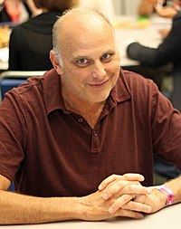 A smiling Caucasian man wearing a red polo shirt.