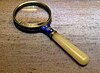 Photo of a magnifying glass with an elegant blue and yellow handle, lying on a wooden surface.