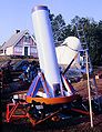 A large trailer mounted newtonian reflector on display during the 1983 Stellafane Convention with the pink Clubhouse and the Porter Turret Telescope in the background