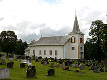 Foto einer weißen Holzkirche mit Grabsteinen im Vordergrund