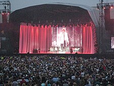 A man, performing on a stage in front of a capacity crowd.