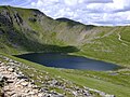 Tu est Hevellyn: Ow mires orth Red Tarn dhyworth Striding Edge, ha topp Helvellyn a-dryv dhodho