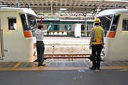 駅で先着列車に後着列車が連結（併合）する写真、左側の駅員が操車係として赤色と緑色の手旗を持って指示し、後着列車運転士に対して停止位置指示、小移動、連結通告、小移動の指示をしてその後連結される。（写真は熱海駅）