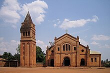 Foto yang menggambarkan gereja Katolik di Rwamagana, Provinsi Timur, termasuk pintu masuk, fasad, menara bel yang terpisah, dan halaman depan yang berdebu.