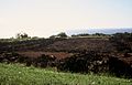 Photograph of the ruins at Puʻu o Mahuka Heiau beneath a cloudless sky with the Pacific Ocean behind.