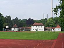 Vue d'un terrain de football devant un bâtiment allongé à la toiture en briques rouges.