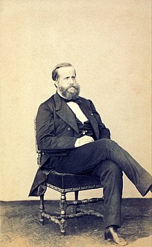 Photograph of a seated, bearded man dressed in a dark suit and vest