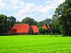 Boerderijcomplex: kop-romp boerderij geflankeerd door twee schuren. Voor het woonhuis is een ijzeren hekwerk en haag.