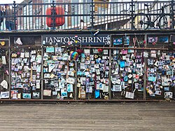 An informal shrine labelled "Ianto's Shrine", with many notes, pictures, and other objects on a brown wall.