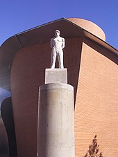 A stone statue of Shakur standing on a tall stone pillar in front of the MARTa Herford museum