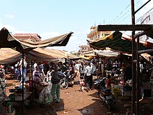 Outdoor market stalls on red earth, with makeshift cloth roofs