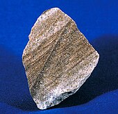 A rough chunk of sandstone with the face showing layering in shades of brown, black and white.