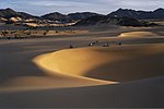 Sand dunes in the desert, offroad vehicles and mountains in the distance.