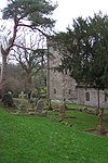 A stone church in a graveyard behind evergreen trees