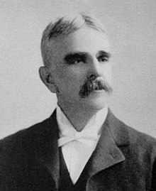 A man with graying hair and a mustache wearing a black jacket and vest and white shirt and bowtie