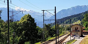 Two-story building with gabled roof situated in mountain valley next to double-track railway line