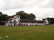 Après un match, une tribune en béton accolée à des bâtiments de style architectural basque et landais.