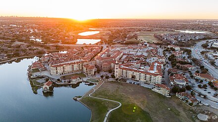 Aerial photograph of Jeff Blackard's Adriatica development with clay tiles roofs, water in the bottom half, a bell tower, and a number of buildings