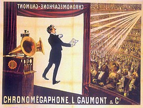 Illustration of a theater from the rear of the stage. At the front of the stage, a screen hangs. In the foreground is a gramophone with two horns. In the background, a large audience is seated at orchestra level and on several balconies. The words "Chronomégaphone" and "Gaumont" appear at both the bottom of the illustration and, in reverse, at the top of the projection screen.