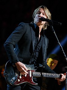 Keith Urban, singing into a microphone while playing an electric guitar