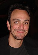 Head shot of broadly smiling man in black with receding dark hair and a day's beard growth on his face.