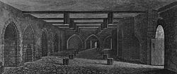 A monochrome illustration of a stone and brick-walled room. An open doorway is to the right. The left wall contains equally spaced arches. The right wall is dominated by a large brick arch. Three arches form the third wall, in the distance. The floor and ceiling is interrupted by regularly spaced hexagonal wooden posts. The ceiling is spaced by wooden beams.