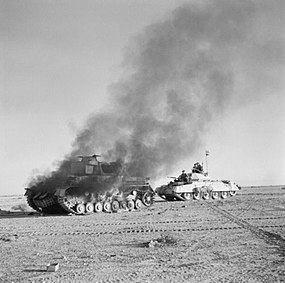 Britský tank Crusader projíždí kolem zničeného německého tanku Panzer IV během Operace Crusader, listopad 1941