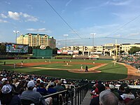 A baseball game on a green field as seen from the seating bowl behind home plate