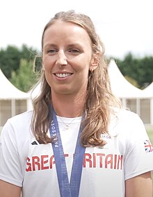 Annie Campbell-Orde trägt ein weißes T-Shirt mit der Aufschrift Great Britain. Um den Hals hängt ein blaues Band, an dem ihre olympische Medaille befestigt ist, die allerdings nicht im Bild zu sehen ist.