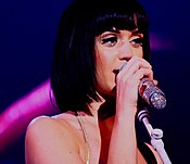 Katy Perry with short, black hair singing into a silver sparkly microphone.