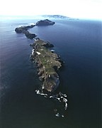 Aerial view of Anacapa with the lighthouse and coastguard station on East Anacapa in the foreground and Middle and West Anacapa behind. Santa Cruz Island is on the horizon.