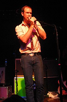 Musician Charles Spearin holding a microphone onstage at a concert in 2008