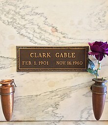 Cripta de mármore com placa de latão inscrita: Clark Gable, 1º de fevereiro de 1901 16 de novembro de 1960. Dois vasos são anexados ao cripta, uma contém uma rosa roxa.