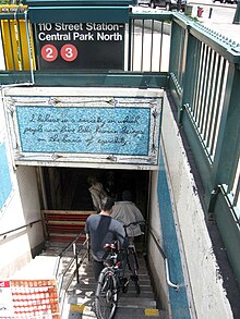 entrée de métro, un escalier descend dans le métro. Un panneau indique Central Park Nord – 110th Street. Sur une mosaïque à fond bleu, on peut lire I believe in a society in which people can live like human beings on the basis of equality.