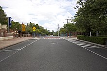 A tree-lined suburban street with red brick buildings to the right.