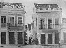 À direita, o segundo endereço da famosa Pharmacia Franceza fundada por Jean Pegot em 1856, que ficava na esquina do Beco do Estudantil, atual Travessa 15 de Novembro com a Rua do Comércio. Na primeira porta à esquerda se lê a chamada de uma loja para a venda de "Machinas de Costura Singer", a alicerçar o destino de Caruaru como futuro polo sulanqueiro.