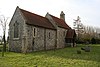 A small flint church with red tiled roofs and a bellcote at the far end