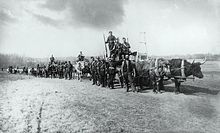 Photographie en noir et blanc de soldats, de gendarmes et d'autres hommes sur des chariots tirés par des bœufs ou se tenant à côté d'eux