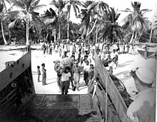 A black and white photo of several people boarding a ship carrying their belongings.