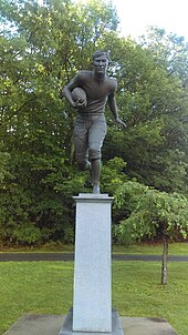 Statue of Jim Thorpe dashing while carrying a football in front of a group of trees