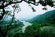 Photographie du système d'irrigation de Dujiangyan. Les voies d'eau sont visibles au fond d'une vallée bordée de montagnes verdoyantes sur la droite.