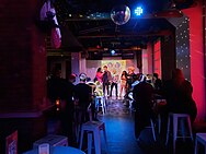 Photo of two drag queens and three patrons on stage at the bar