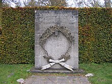 Stele grigia di pietra fittamente scolpita con decine e decine di nomi, appoggiata alla stele una fronda di quercia in bronzo.