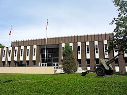 Photo en couleur de la façade d'un bâtiment brun avec une porte vitrée au centre surmontée d'un insigne militaire