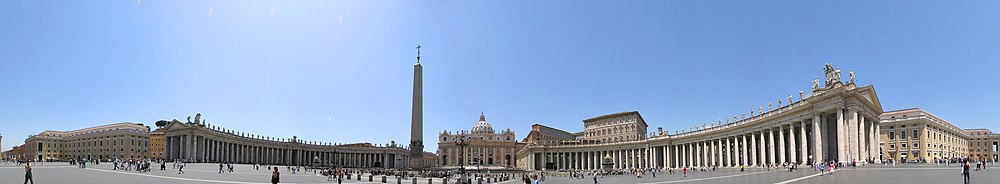 Panorama showing the façade of St. Peter's at the centre with the arms of Bernini's colonnade sweeping out on either side. It is midday and tourists are walking and taking photographs.