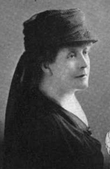 An older white woman wearing a dark brimmed hat with a veil in back